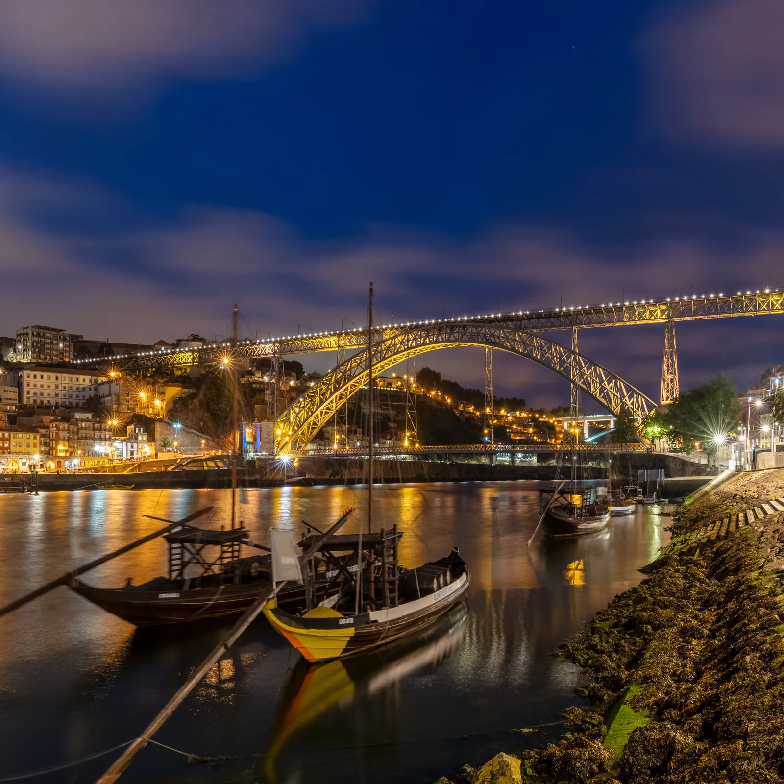 Wooden rabelo boats on the Douro below the lit Dom Luís I bridge in Porto at dusk