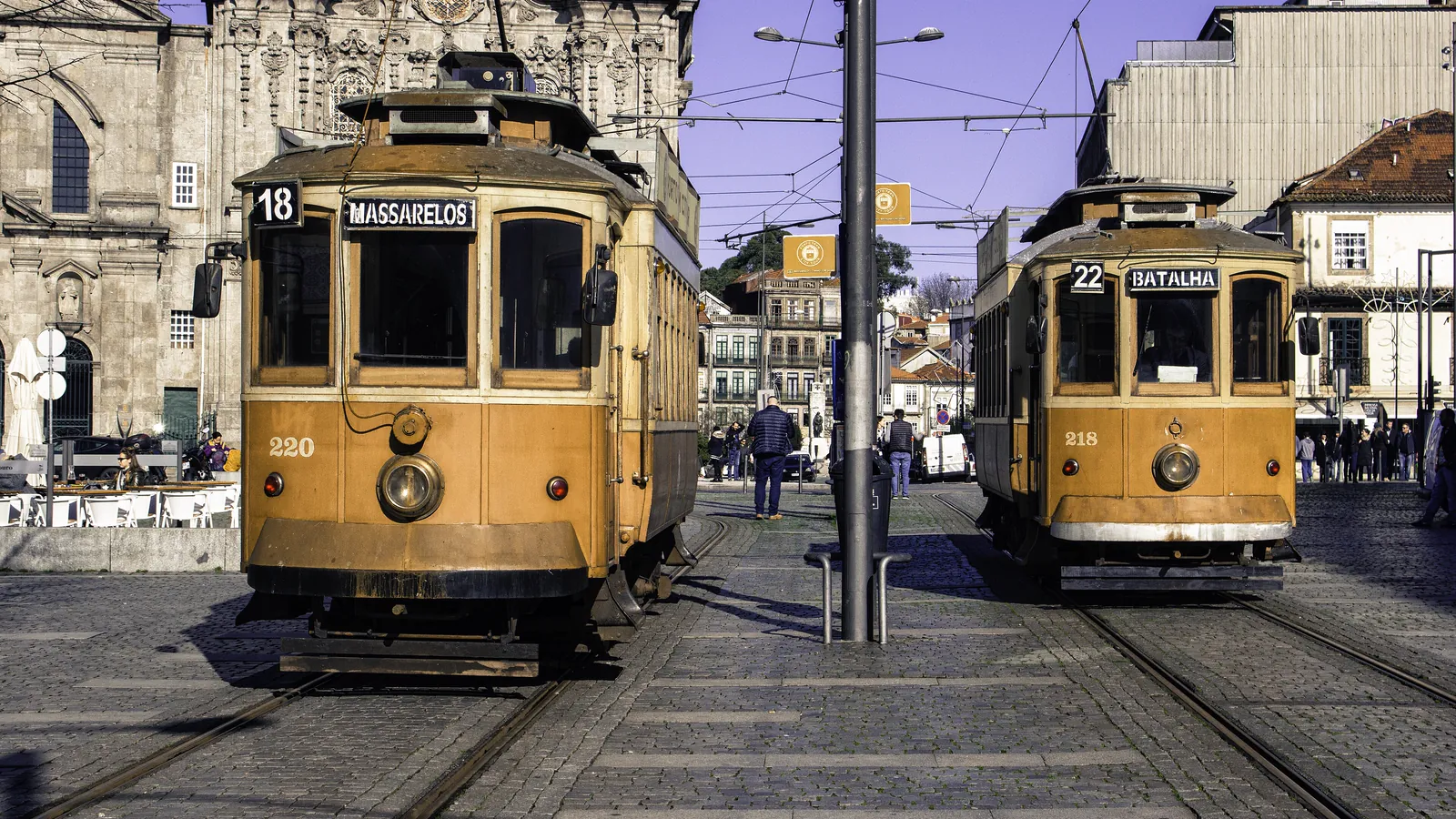 Two of Porto's old yellow trams side by side in a cobbled square